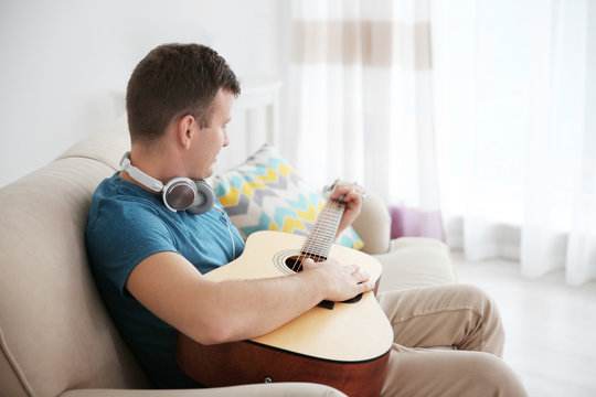 Young man with headphones playing guitar and sitting on the couch