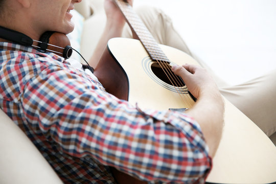 Closeup of young man playing the guitar in a light interior