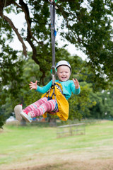 Laughing blonde child in helmet hangs from zip line