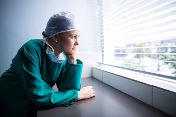 Thoughtful female surgeon looking through window