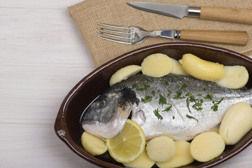 A pan with raw fish standing near fork and knife. Horizontal studio shot