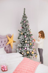 Portrait of cute happy little girl helping her family to decorate Christmas tree in living room. Child hanging holiday decorations. Vertical color photography.