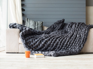 Merino wool grey blanket lying on white sofa with an orange cup