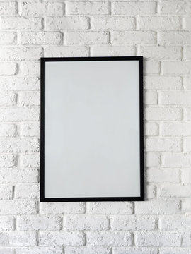 Photo of poster in a black frame on a white brick wall. Empty space for text.