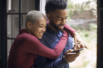 Happy couple using mobile phone while standing in doorway