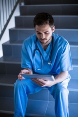 Male nurse sitting on staircase and using digital tablet
