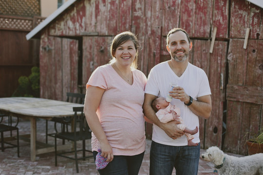 Portrait Of Smiling Woman And Man With Baby Girl And Dog In Yard