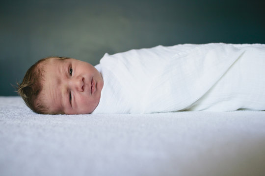 Close Up Of New Born Baby Wrapped In Sheet Lying On Bed