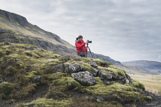 Man photographing while standing on hill against cloudy sky