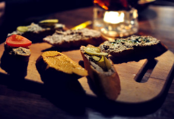 Toasted bread with pate, salmon and vegetables on wooden cutting board in a restaurant. Six different sandwiches, variety of flavors.
