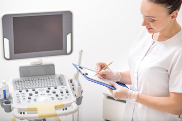 Fototapeta na wymiar Cosmetologist making notes near ultrasound device