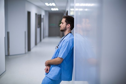Tensed male nurse leaning on wall in corridor