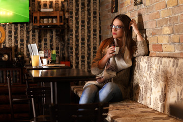 Pensive female student sitting in a cafe and resting while drinking second coffee in a row coffee.