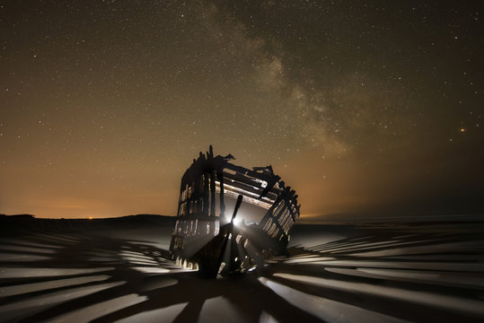 Illuminated Peter Airedale ship on sand against starry sky at night