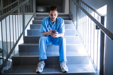 Male nurse sitting on staircase and using mobile phone