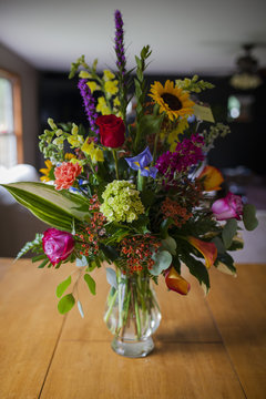 Various flowers in glass vase on wooden table at home