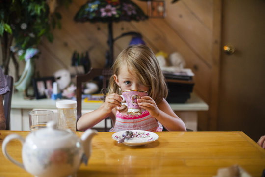 Portrait Of Girl Drinking Coffee While Sitting At Wooden Table