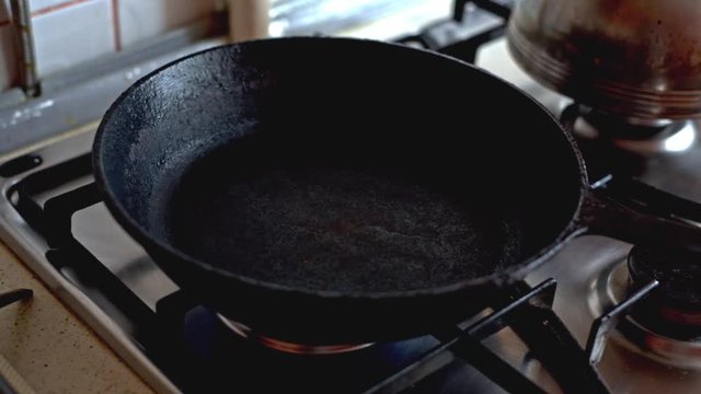 Hand puts the frying pan on a gas stove. Cooking omelette from two eggs.