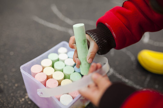 Cropped image of boy playing with chalks on street