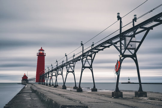 Transmission tower  and lighthouse on pier amidst sea against cloudy sky
