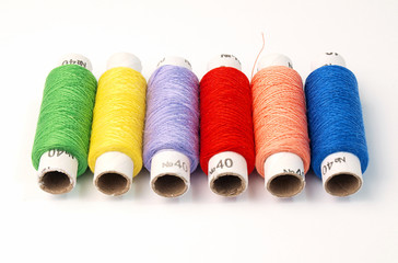 colored coils of sewing threads are in an even number on a white background