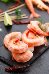 Tasty boiled shrimps with skewers on a stone plate with lime and salad.