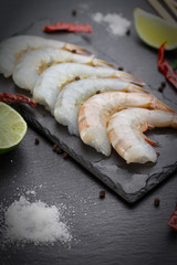 Raw and boiled shrimps on a stone plate on a black table.