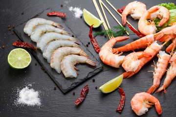 Raw and boiled shrimps on a stone plate on a black table.
