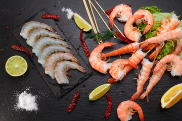 Raw and boiled shrimps on a stone plate on a black table.