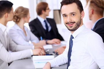 Portrait of cheerful smiling businessman  against a group of  people at meeting.
