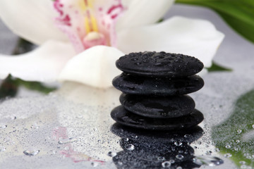 Spa background. Volcanic rock, bamboo and orchids on reflective background with raindrops. Relaxation, body care treatment, spa, wellness concept