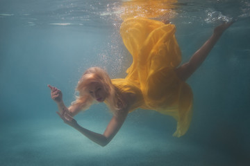 Woman in yellow dress swimming underwater in the pool.