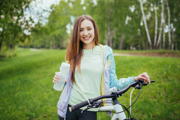 Fototapeta na wymiar Happy girl cyclist standing with a mountain bike and drinking water. Adventure travel. Girl cyclist. Mountain bike. healthy lifestyle. Sort concept.