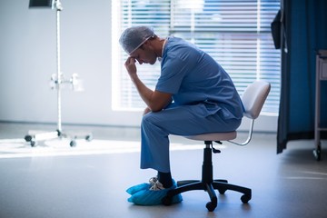 Tensed male nurse sitting in corridor