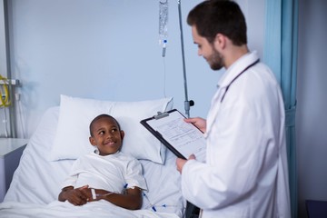 Doctor reading report while patient sleeping on bed