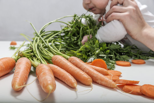 Hands of mother holding a child playing with a bunch of fresh juicy carrots