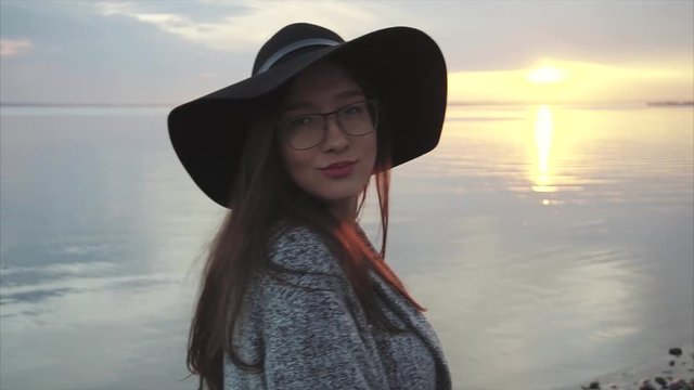 Young pretty woman in black hat and glasses near the sea at sunset HD