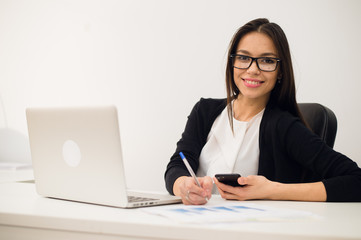 Portrait of businesswoman with laptop writes on a document at her office