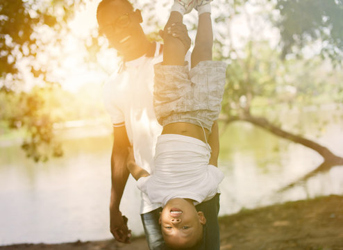 Dad holding a son upside down in park under sunlight - Powered by Adobe