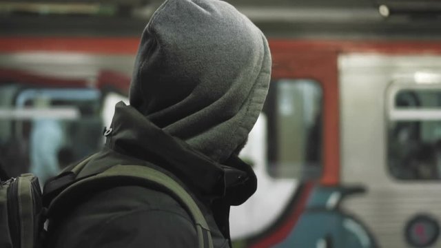 MIllenial youth in hoodie at the train station at night, slomo 100p.A hooded young man is waiting for the train or walking along the platform with or witout his hoodie on, at night.