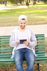 Fototapeta premium Young man using tablet sitting on park bench.
