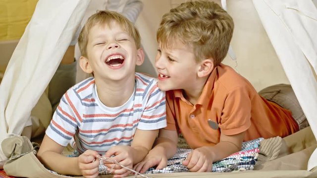 Little boy lying in teepee with laughing friend and telling him jokes