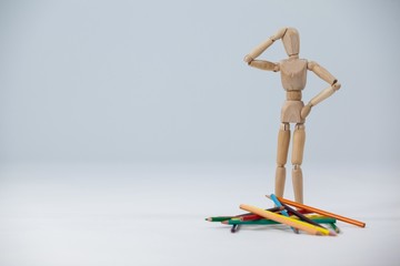 Confused wooden figurine standing near a heap of color pencils
