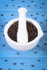 Black pepper in white mortar on blue boards