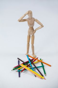 Confused wooden figurine standing near a heap of color pencils
