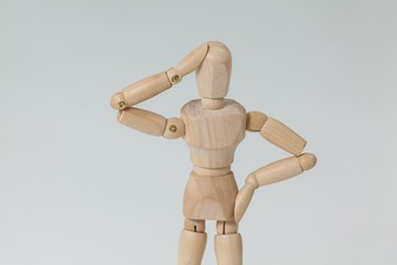 Confused wooden figurine standing with hand on head