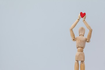 Wooden figurine standing and holding a red heart on top 