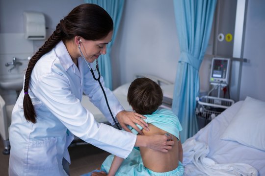 Female doctor examining patient with stethoscope in ward