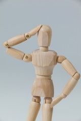 Confused wooden figurine standing with hand on head