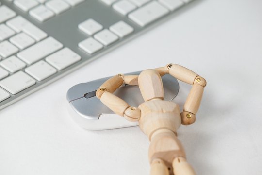 Wooden figurine leaning on mouse beside a keyboard